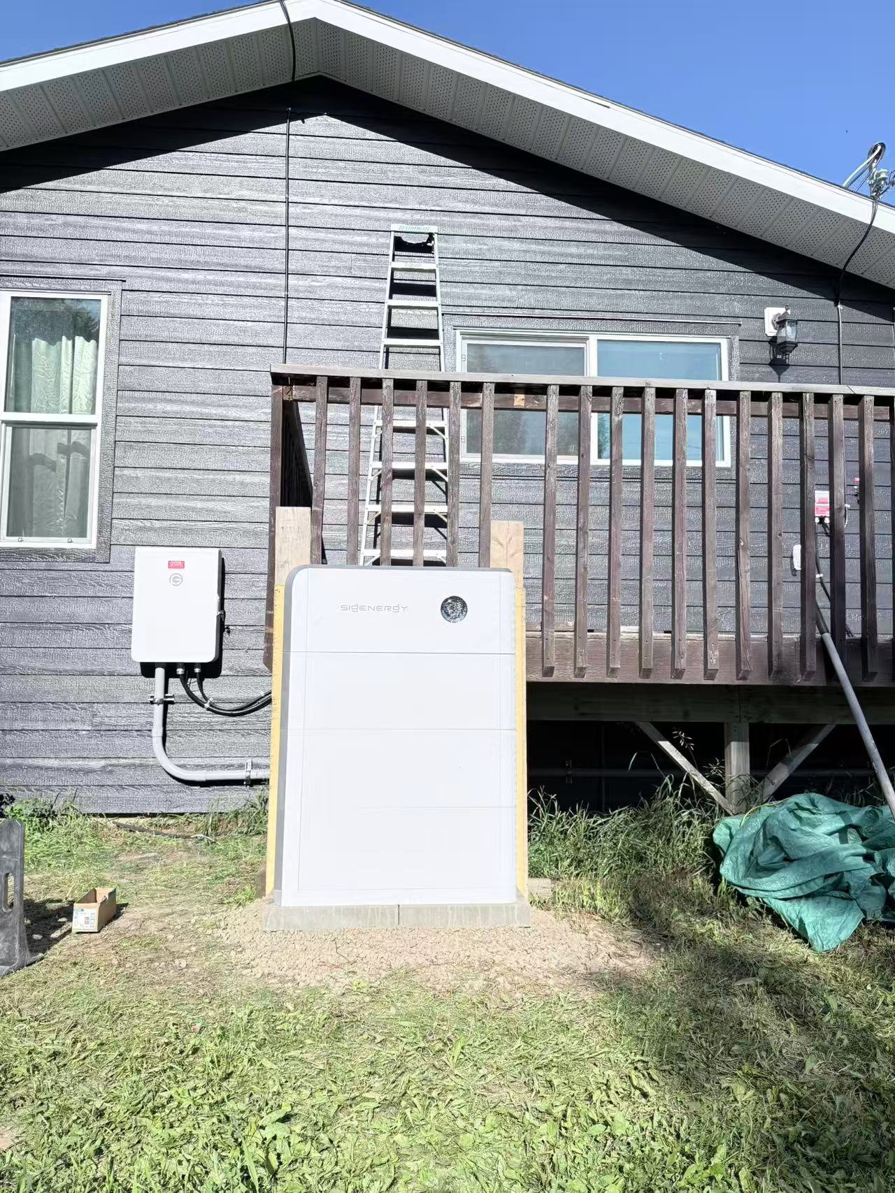 Battery storage system installed beside the deck of a grey house