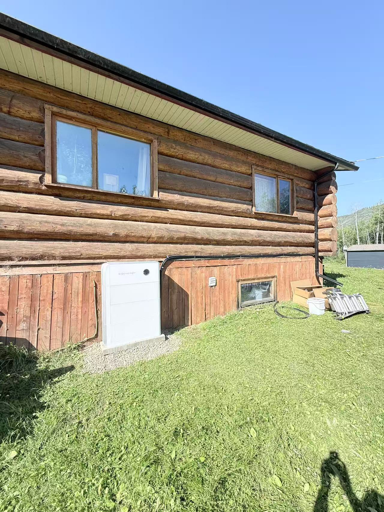White home battery installed beside a log cabin