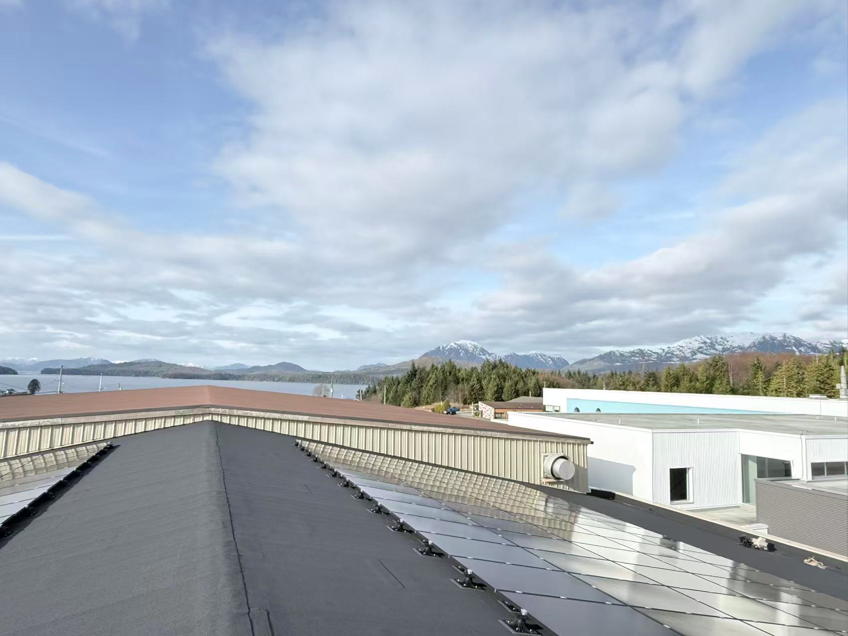 Large solar array covering a commercial rooftop beneath a mountain skyline